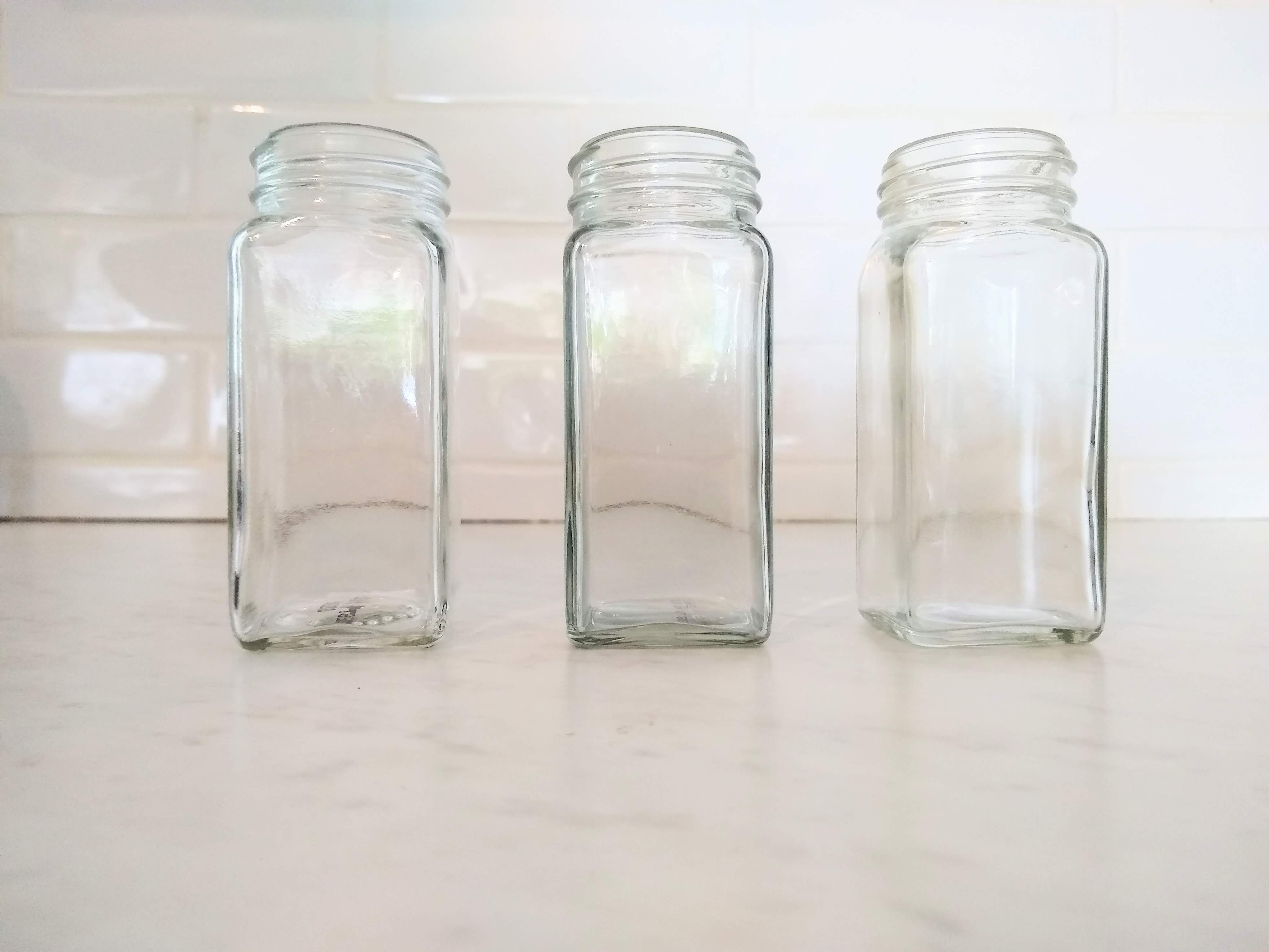 Three empty glass spice jars on a white counter